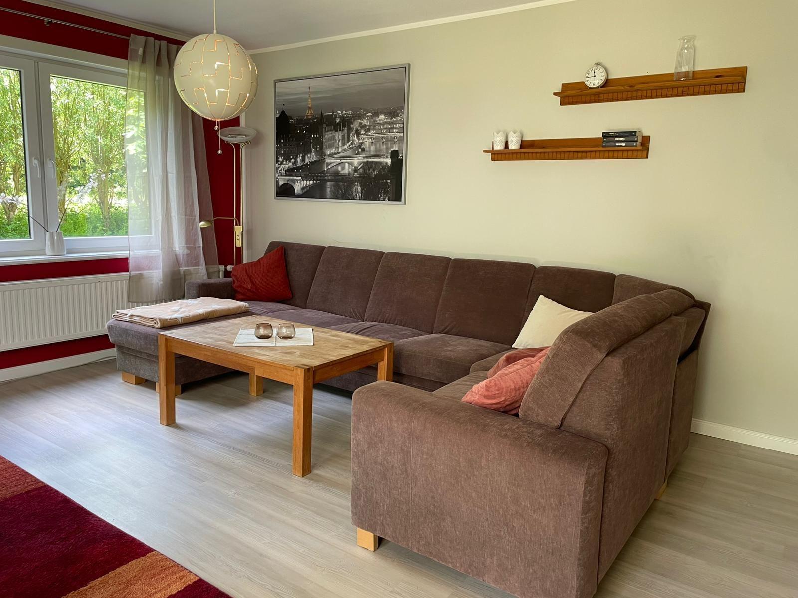 Wohnzimmer mit braunem Sofa, Holztisch und Wandbild. Fenster mit Blick auf Garten.