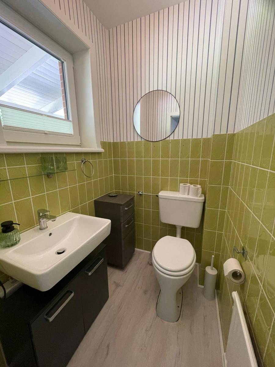 Badezimmer mit grünen Fliesen, Waschbecken, Toilette und runden Spiegel