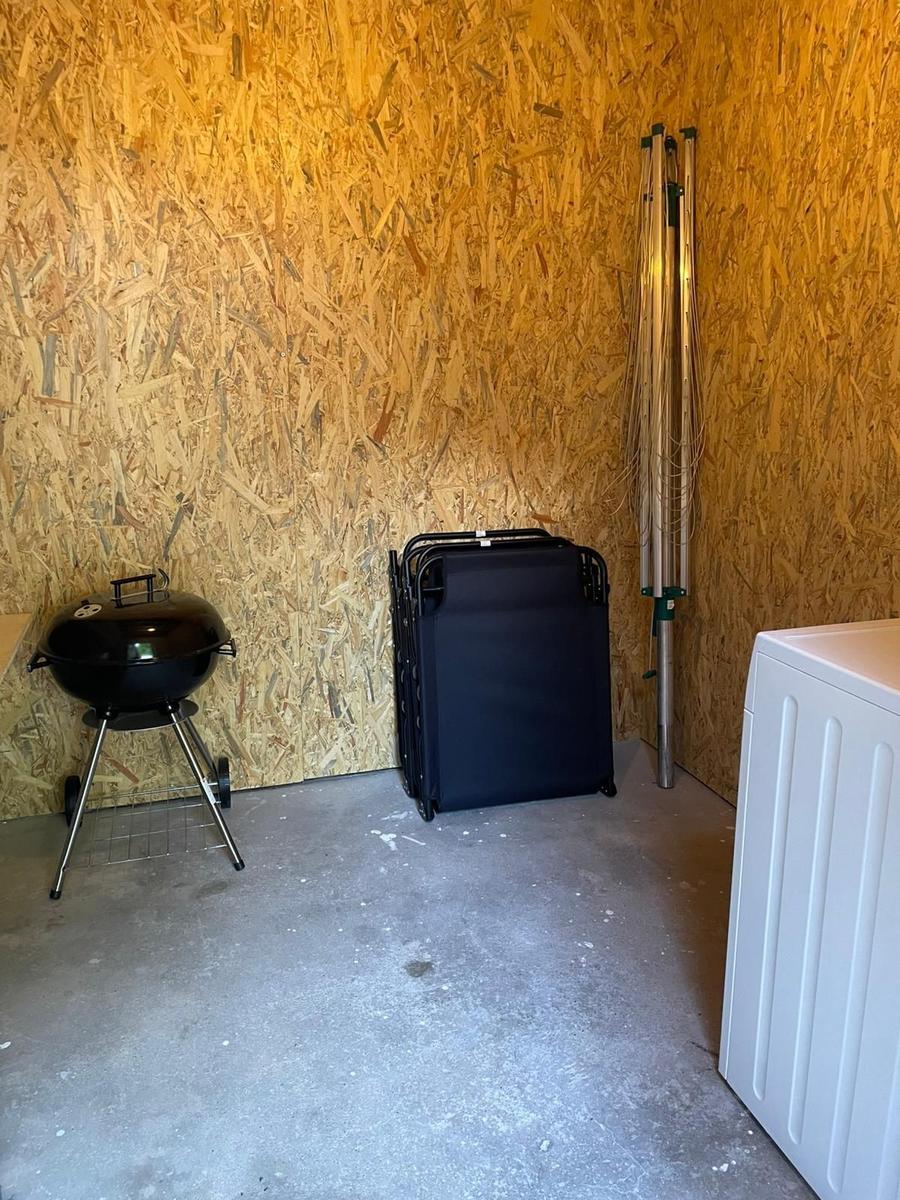 Kleine Garage mit Grill, Klappstühlen und Waschmaschine an OSB-Wand.