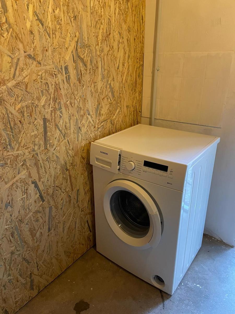 Eine Waschmaschine steht in einem Raum mit OSB-Wand und Fliesenwand.