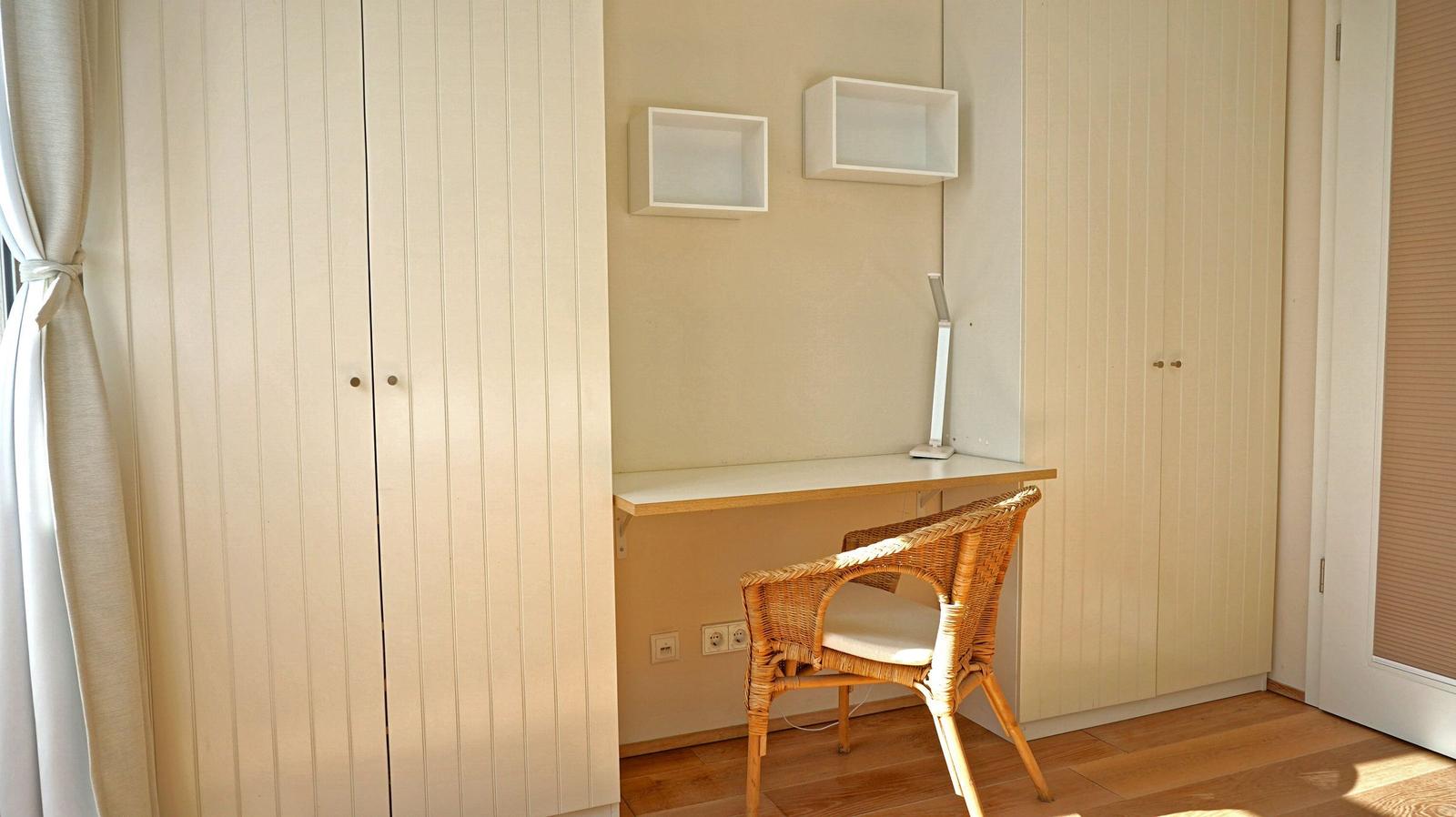 Work desk with chair and wall shelves. Wooden floor and wardrobe wall.