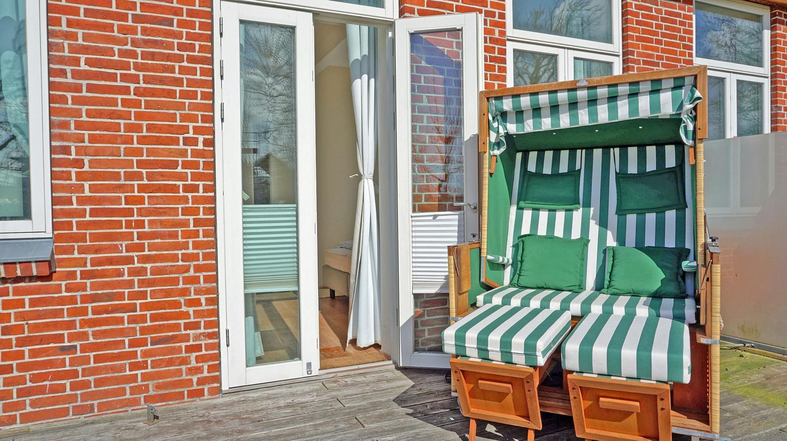 Deck with green-and-white striped lounge and wooden frame in front of red brick house.