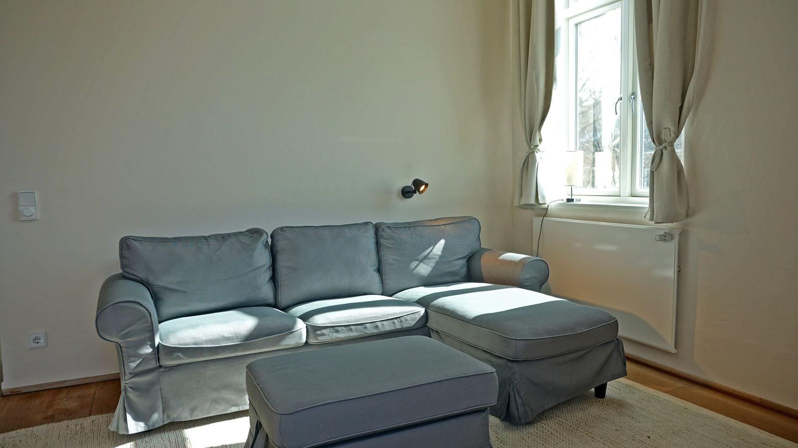 A gray sofa with cushions and footrest stands by a window.