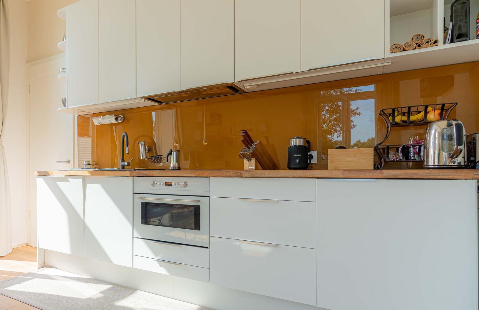 Modern kitchen with white cabinets, wooden countertop, and orange backsplash.