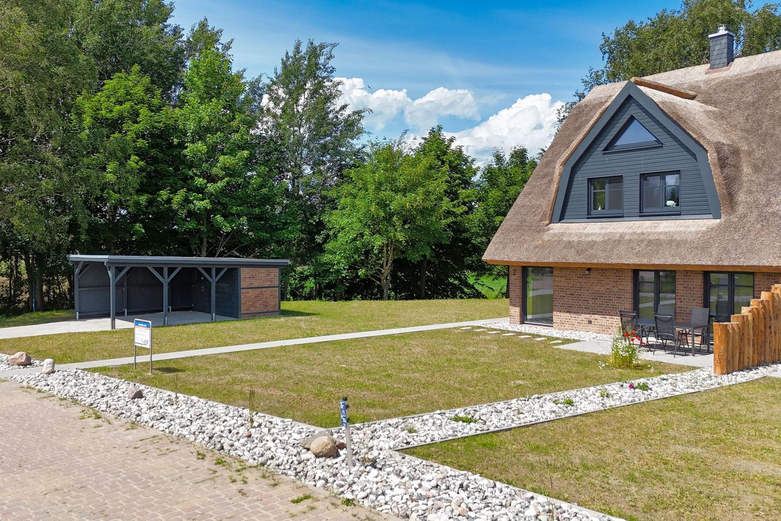 Haus mit Strohdach, Garten und Terrasse mit Sitzgelegenheiten.