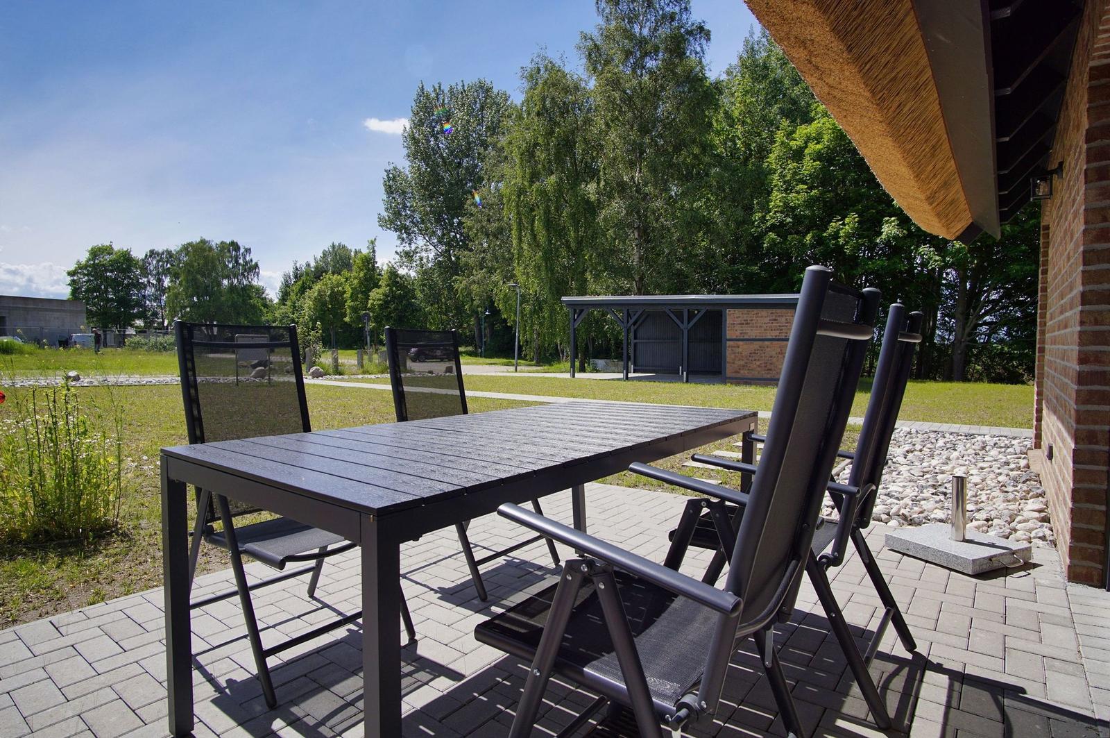 Terrasse mit Tisch und Stühlen, Grünfläche und Bäume im Hintergrund.