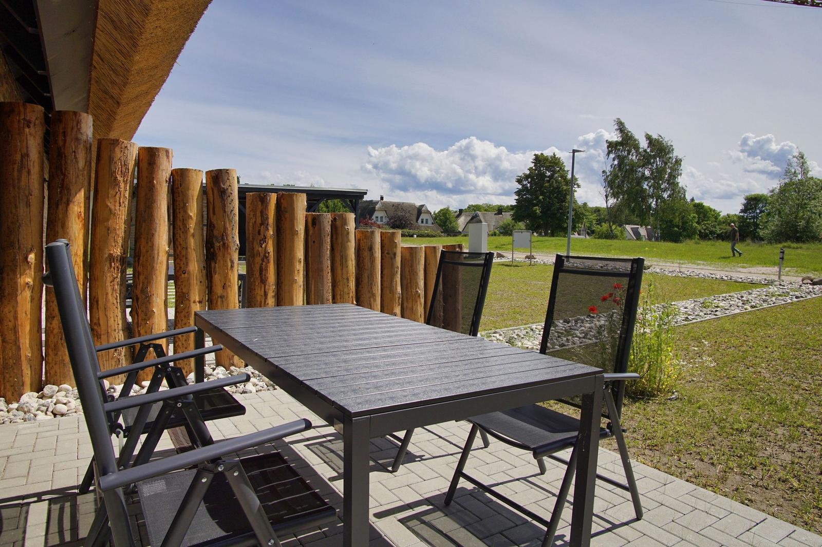 Terrasse mit Tisch und Stühlen, Holzgeländer, Blick auf Grünfläche und Himmel.