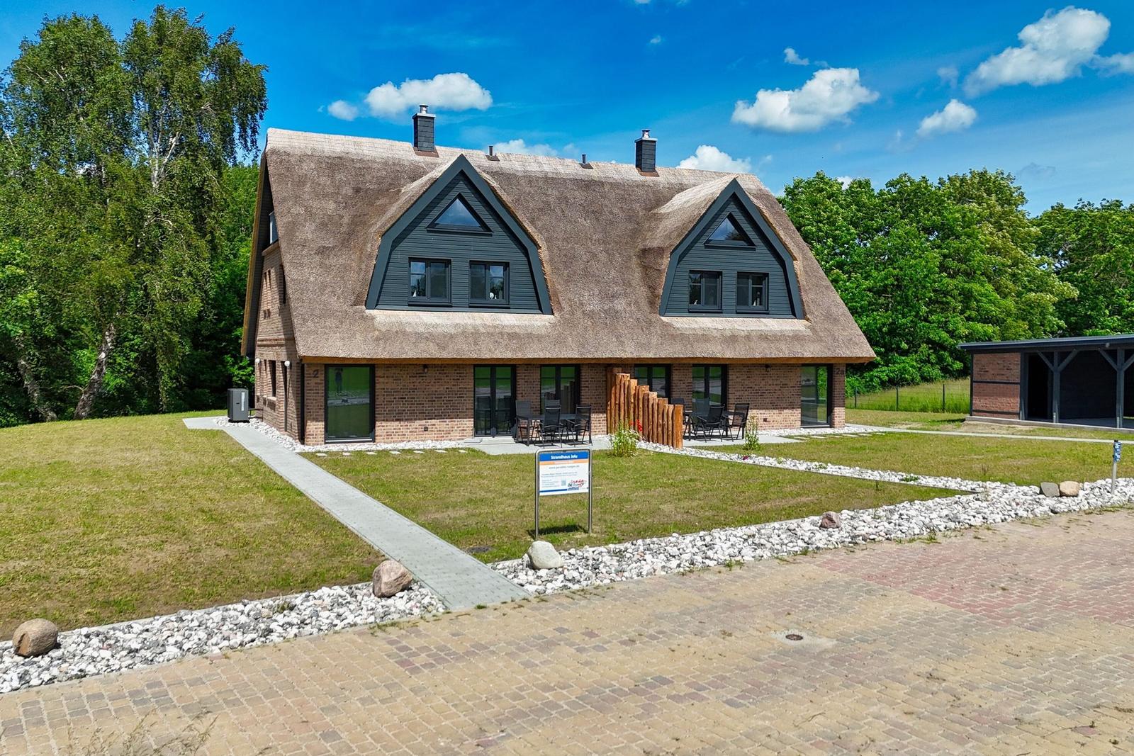 Haus mit Strohdach, Terrasse und Garten. Modernes Design mit Holz und Stein.