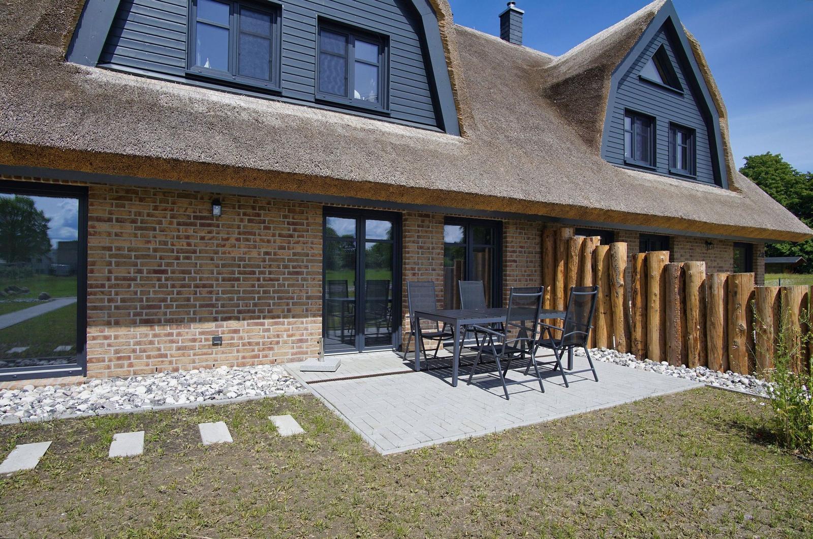 Haus mit Strohdach, Terrasse mit Tisch und Stühlen, Holzumrandung und Steinweg.