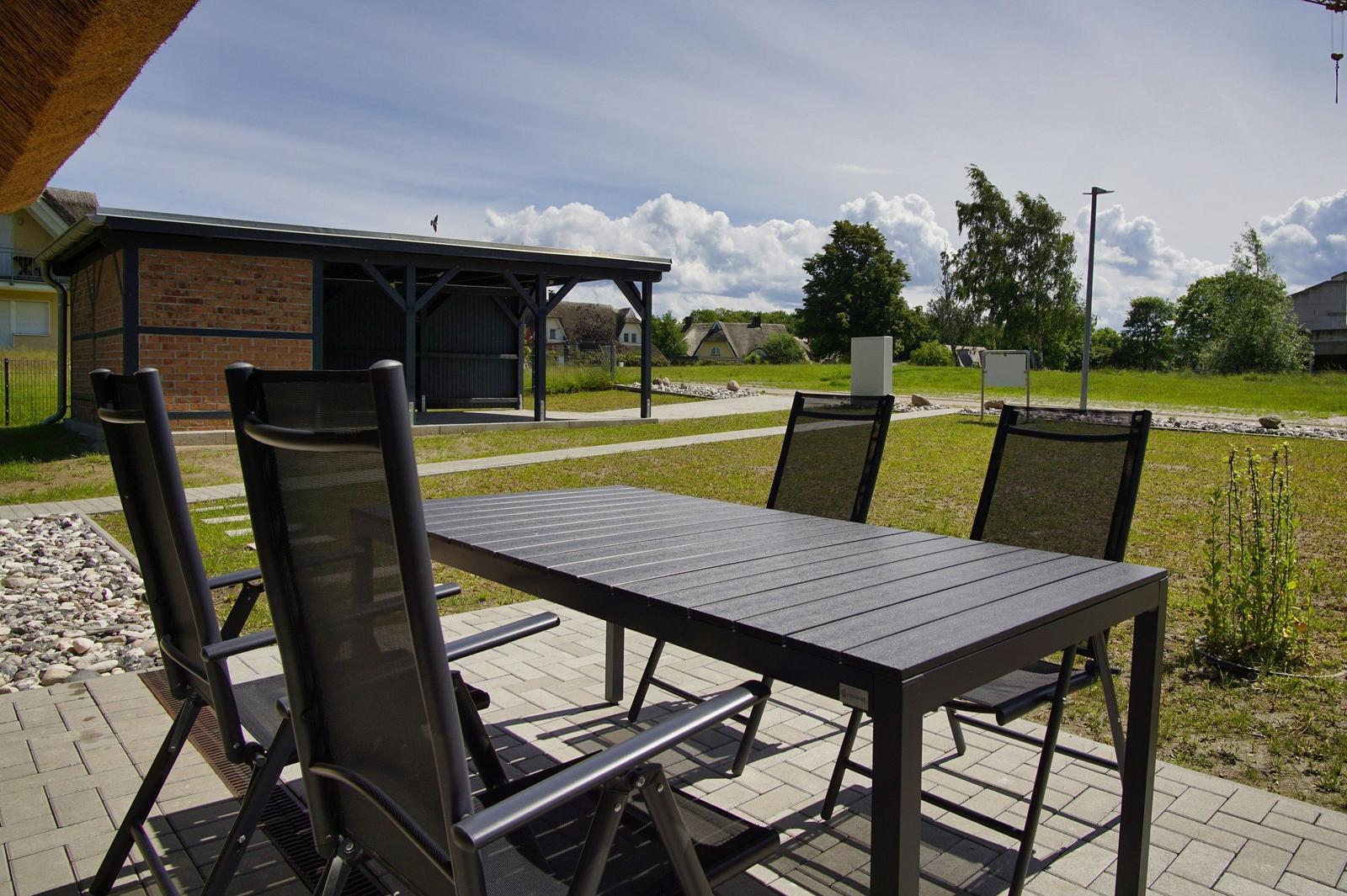 Terrasse mit Tisch und Stühlen. Hintergrund: Garten, Gebäude und Himmel.