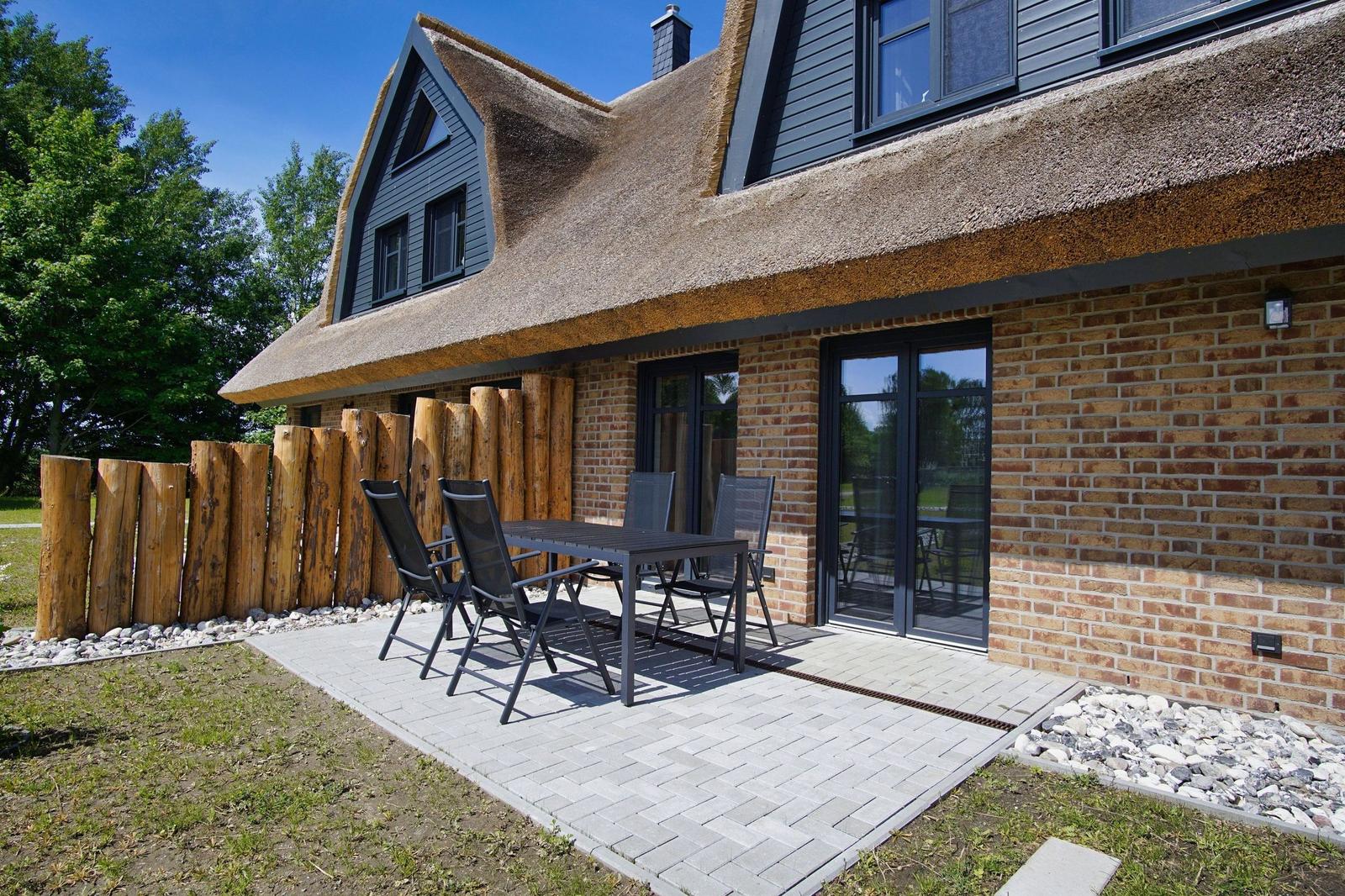 Haus mit Strohdach, Terrasse mit Tisch und Stühlen, Holzzaun und Steinmauer.