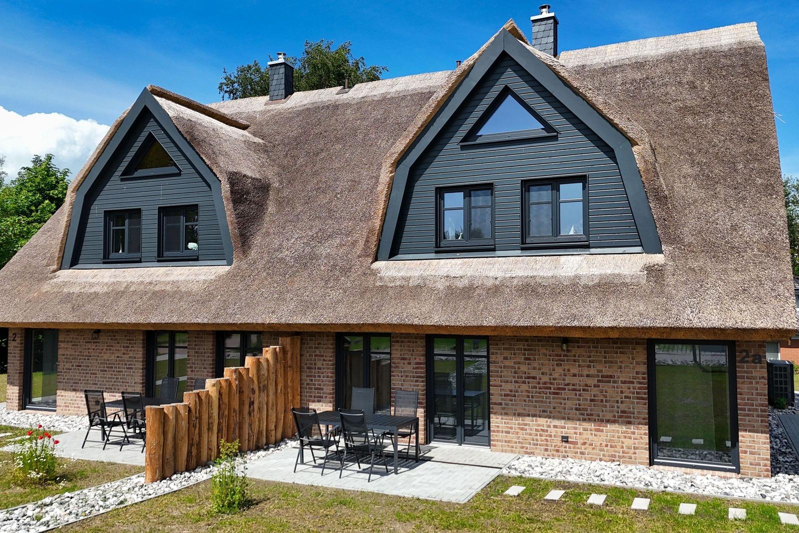 Haus mit Strohdach, Steinmauern und Terrasse mit Tischen und Stühlen.