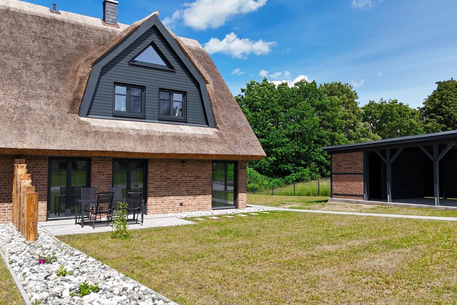 Haus mit Strohdach, Terrasse und Garten. Nebenhaus mit Holzkonstruktion.