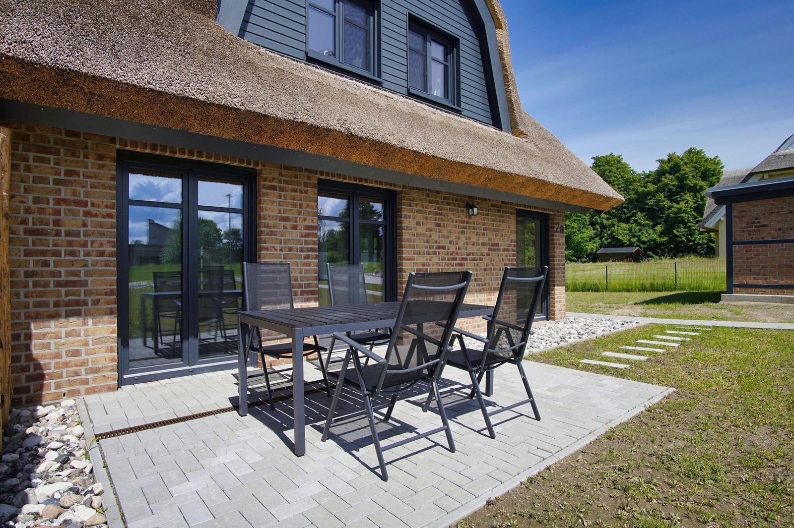 Terrasse mit Tisch und Stühlen vor einem Haus mit Dach und Fenstern.