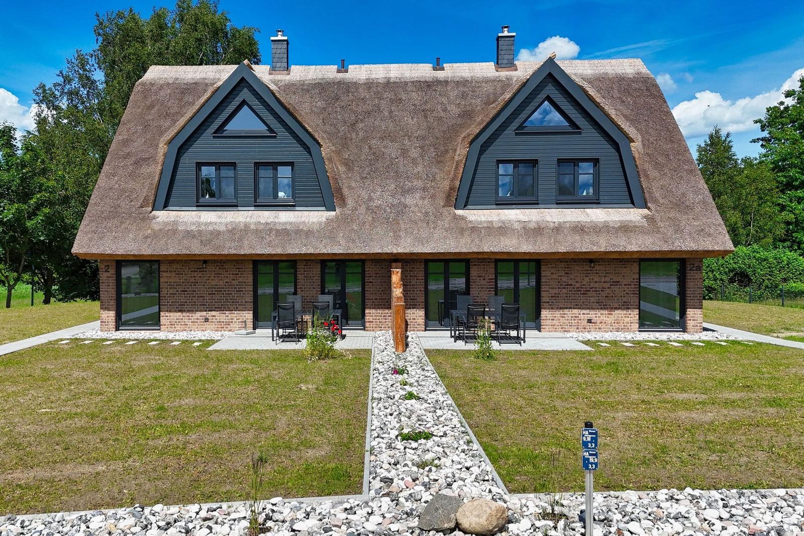 Modernes Haus mit Strohdach und Glasfront, Garten mit Sitzgelegenheiten.