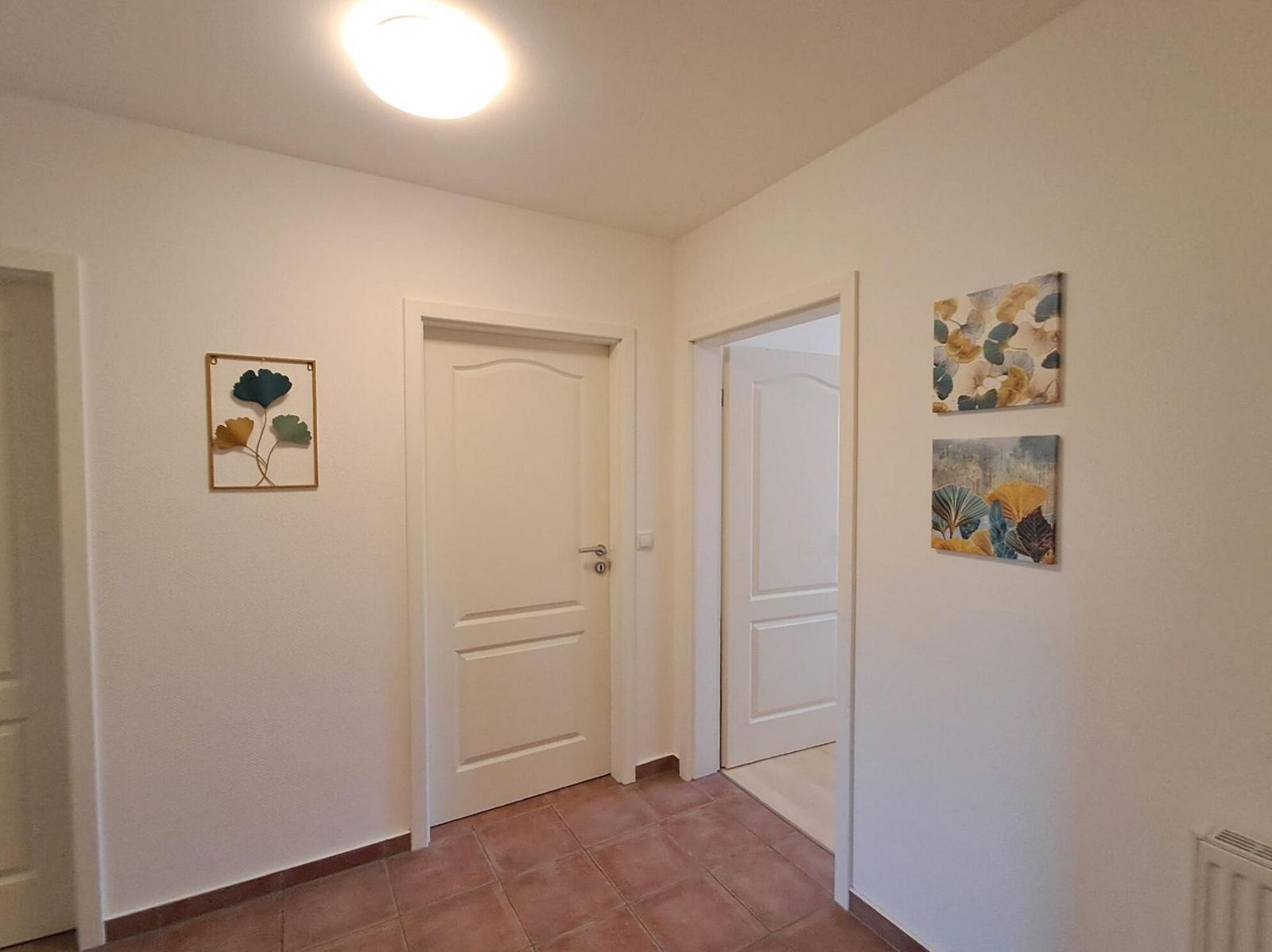 Flur mit drei Türen, Terrakottaboden und Wandbildern mit Blättern.