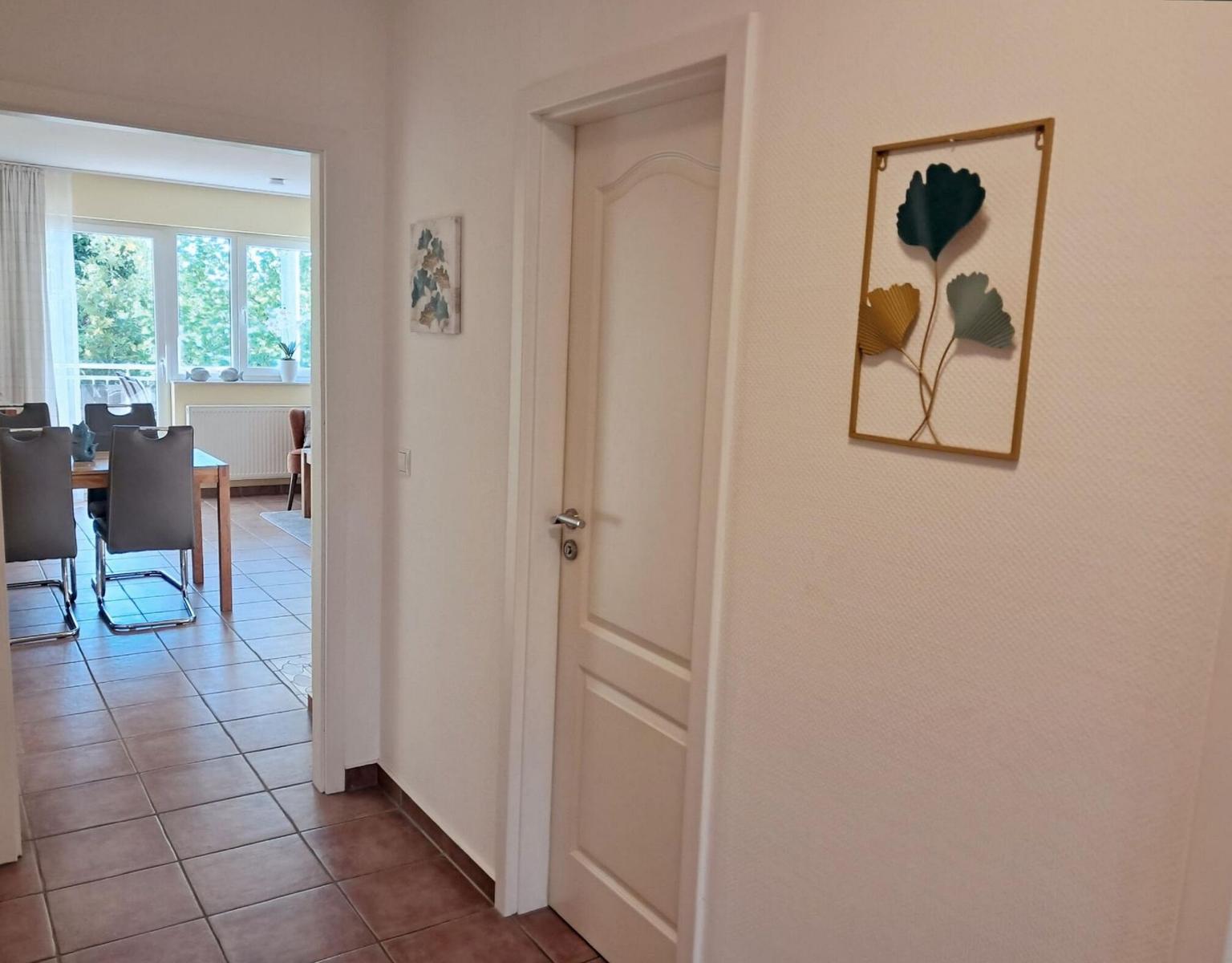 Flur mit Tür und Wandbild, Blick in Esszimmer mit Tisch und Stühlen.