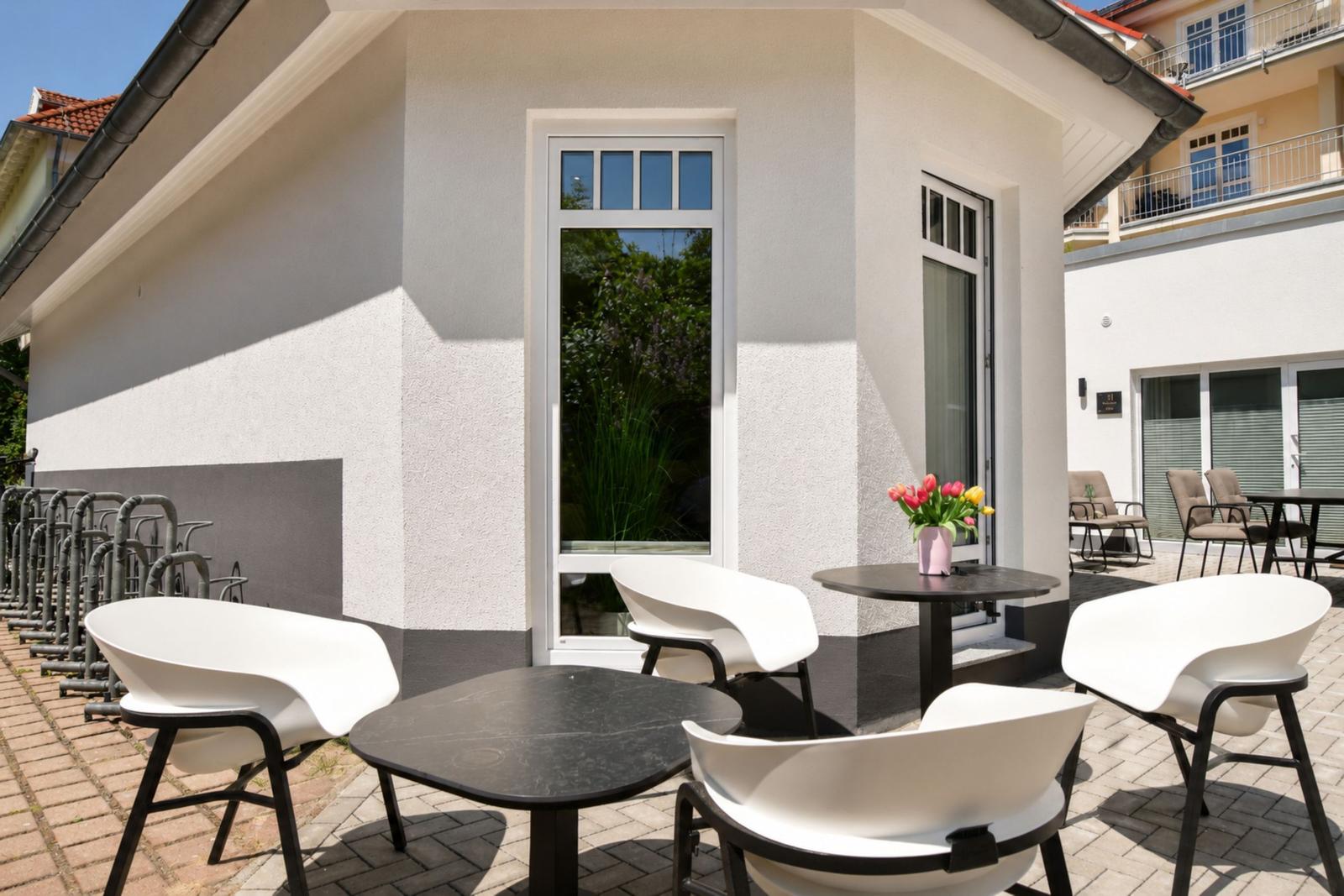 Terrasse mit Tischen und Stühlen, Blumen und Fenster zur Gartenseite.