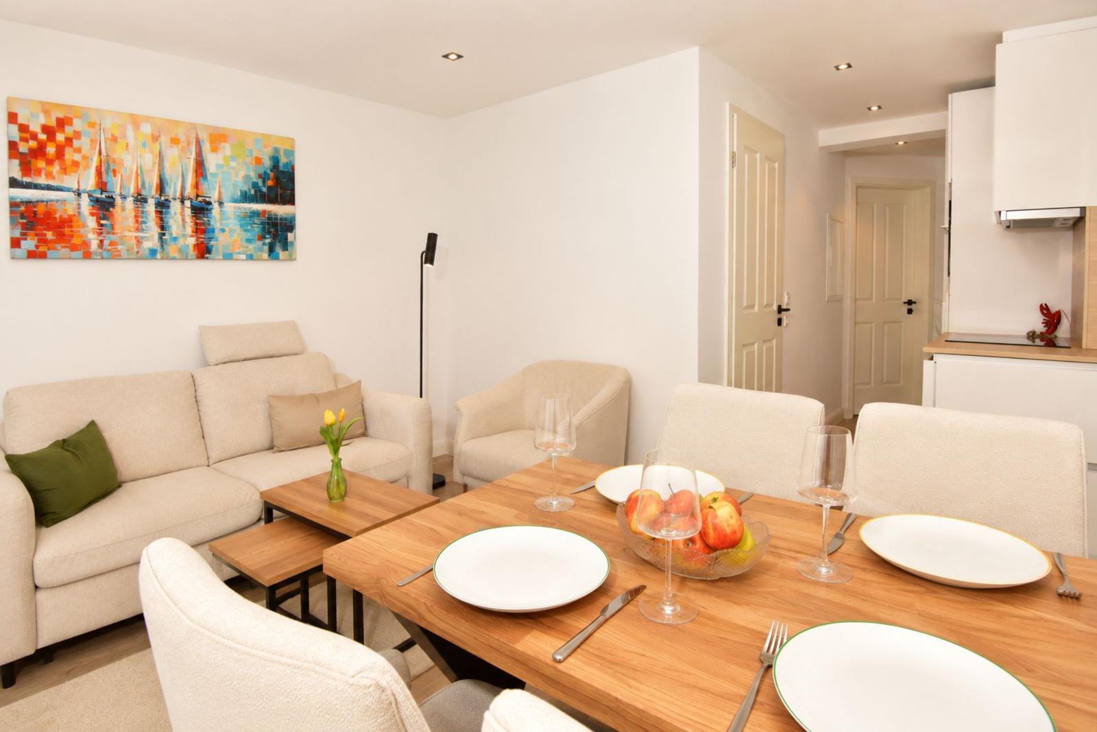Esszimmer mit Holztisch, Stühlen und Früchten. Wohnbereich mit Sofa und Wandbild.