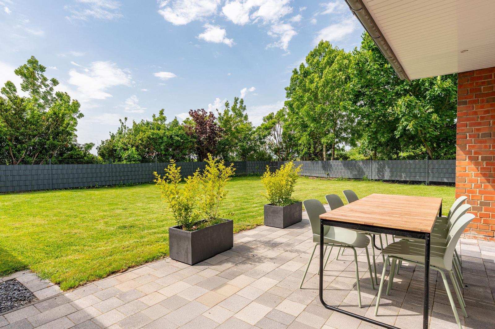 Terrasse mit Tisch und Stühlen, Rasenfläche und Pflanzen in Betonkübeln.