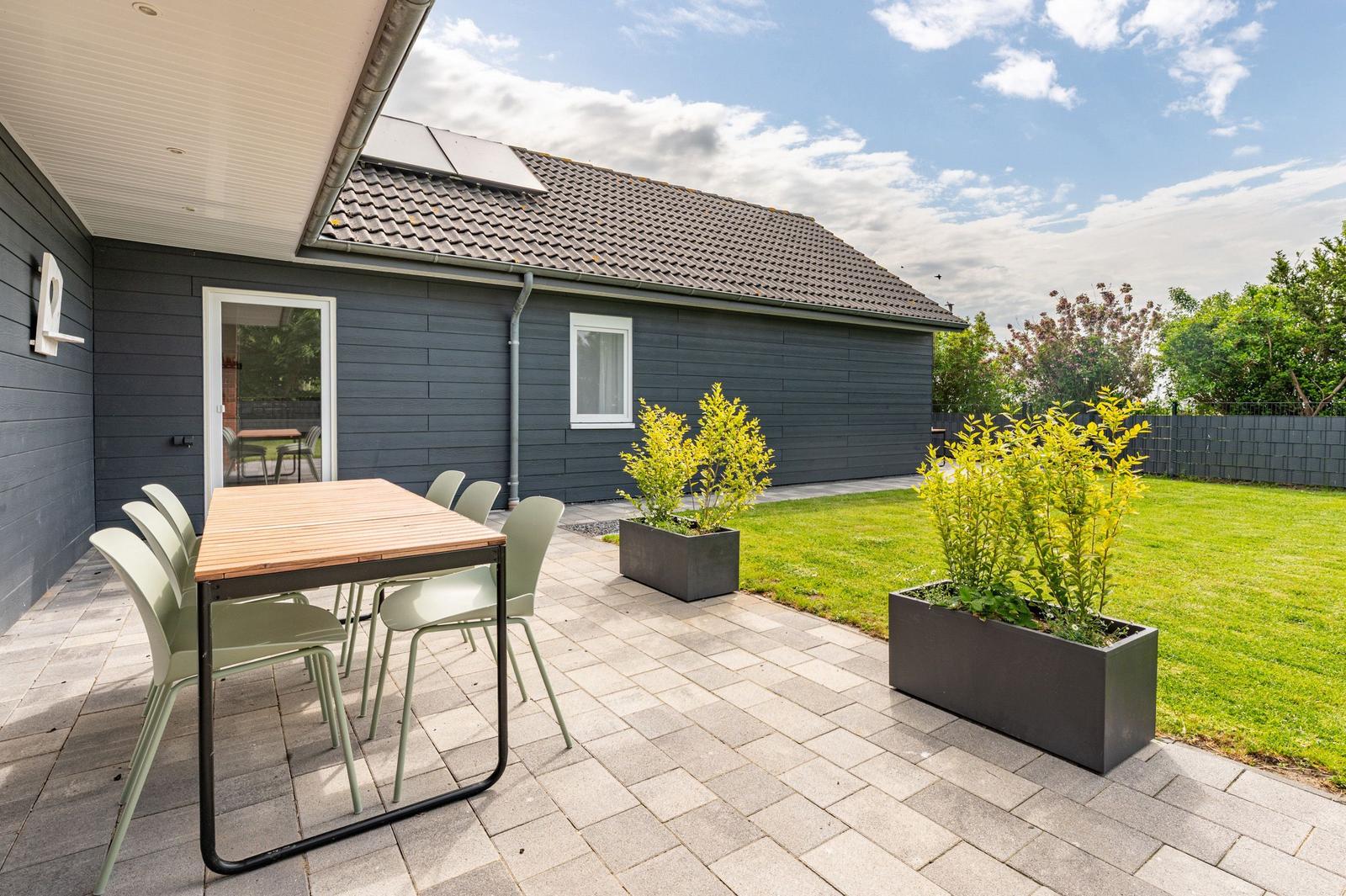 Terrasse mit Tisch und Stühlen, Garten mit Rasen und Pflanzenkästen.