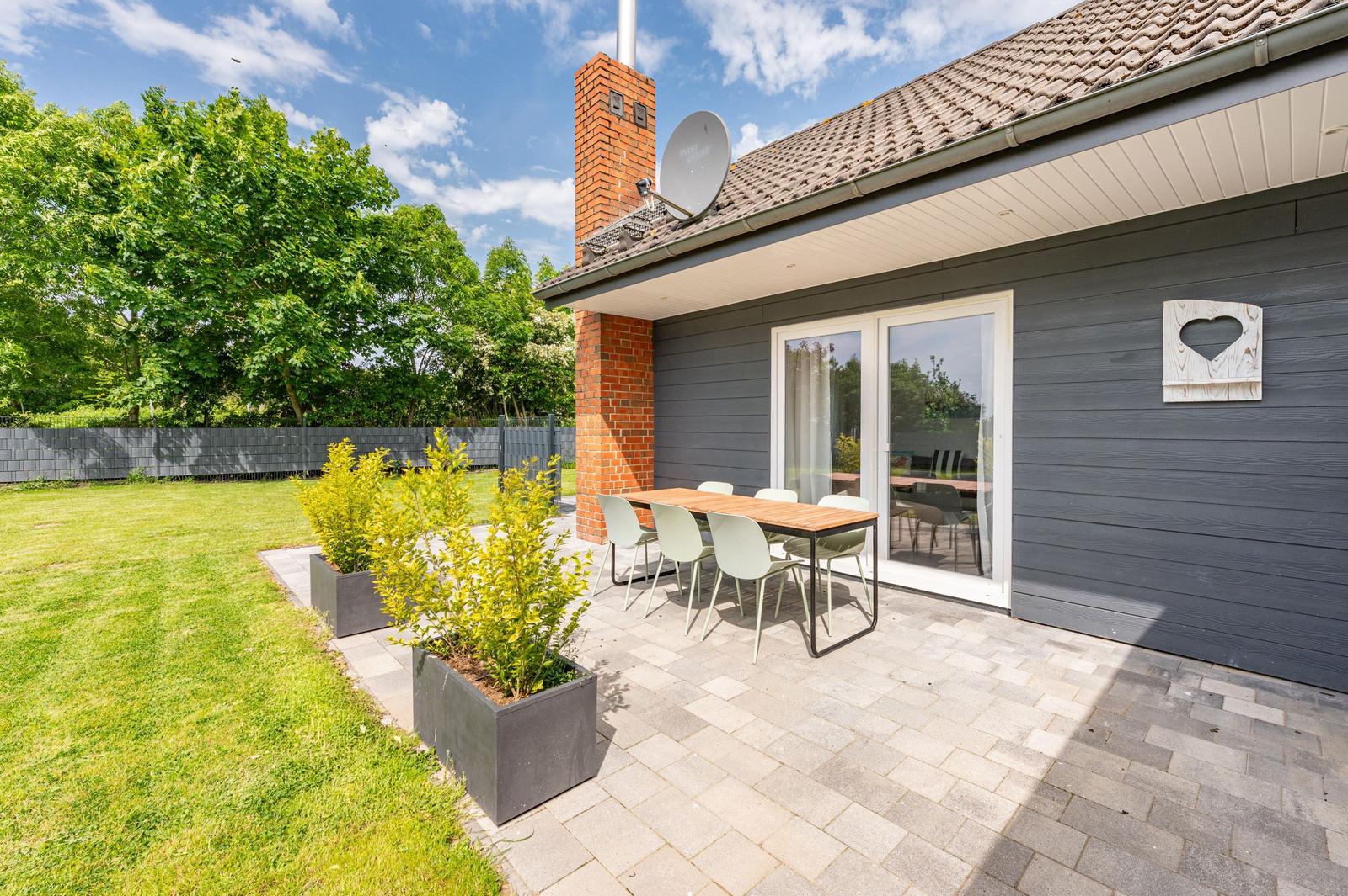 Terrasse mit Tisch und Stühlen, Garten und Satellitenschüssel an Hauswand.