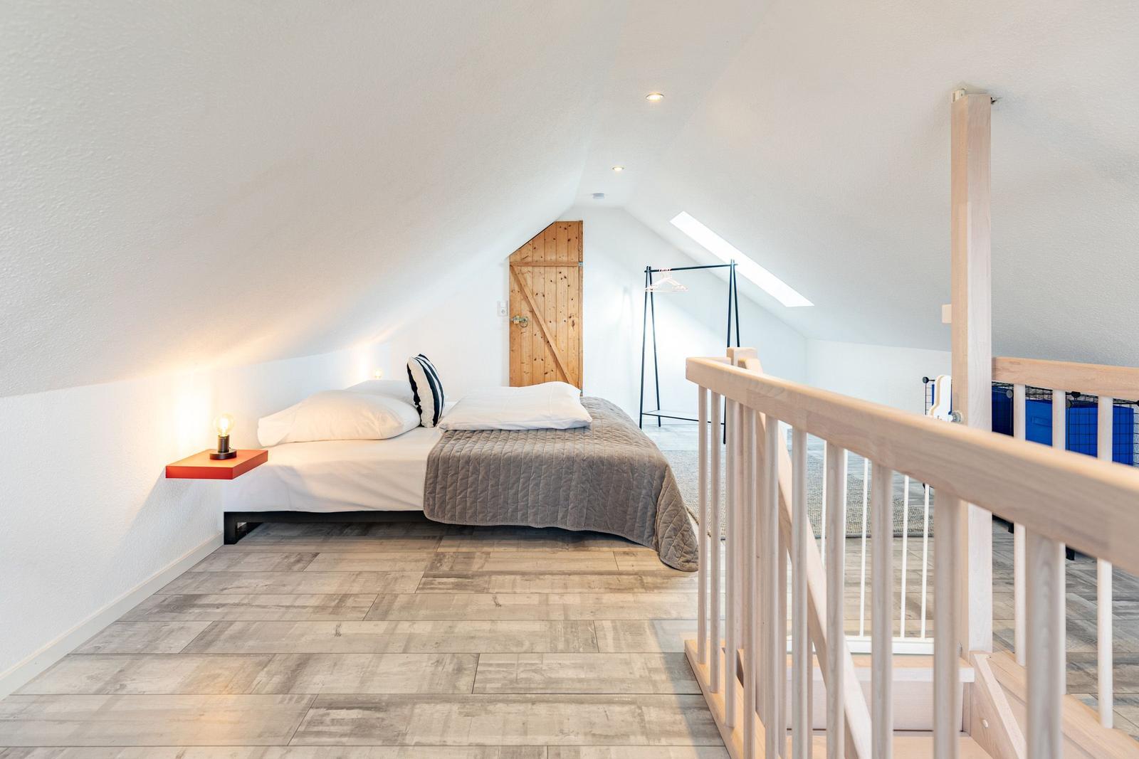 Bedroom with sloped ceiling, bed, nightstand, and clothing rack.