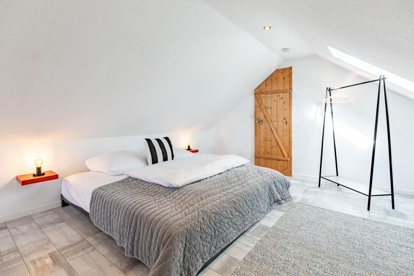 Bedroom with bed, clothing rack, and wooden door under sloped ceiling.
