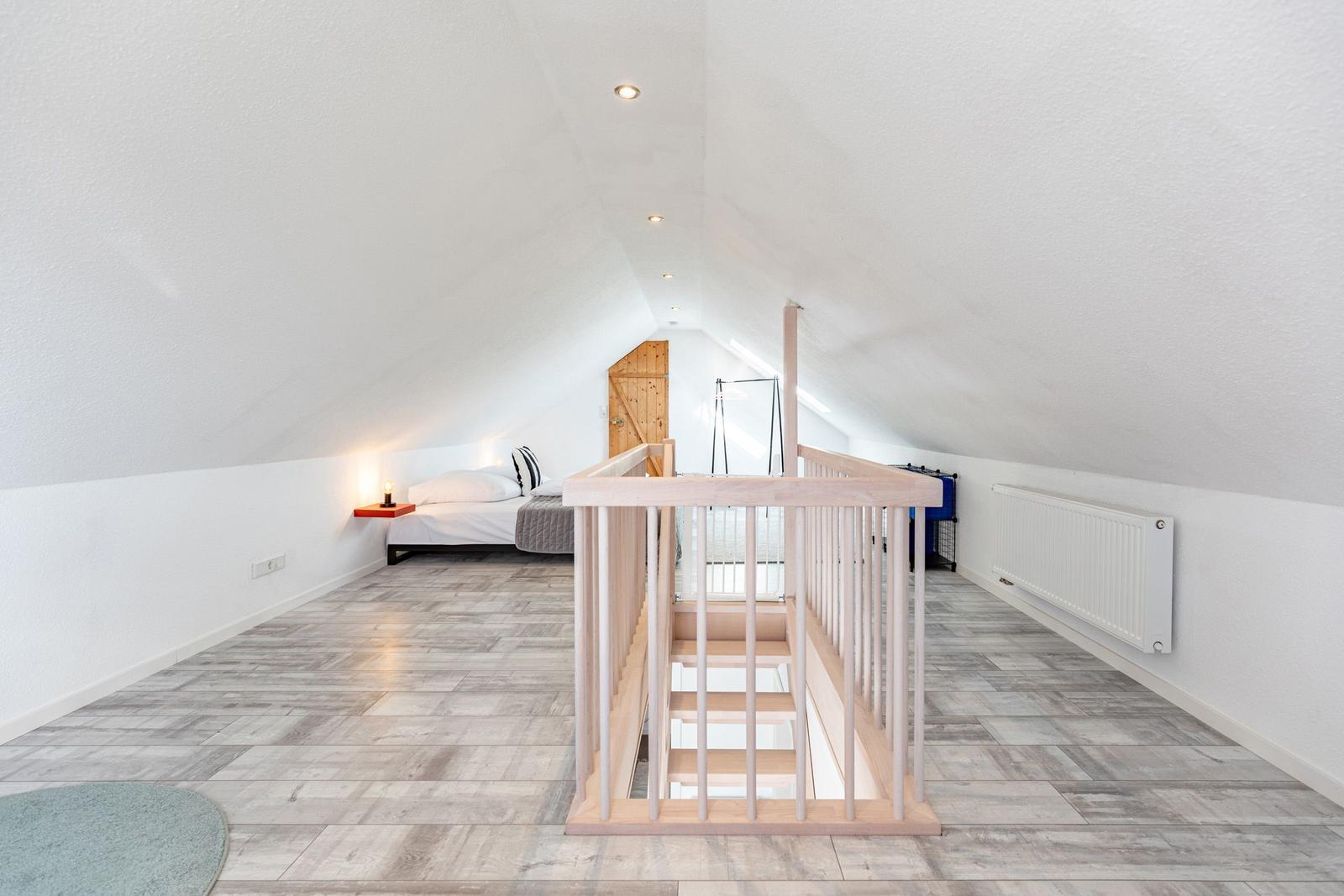 Attic room with bed, wooden railing, and wooden floor.
