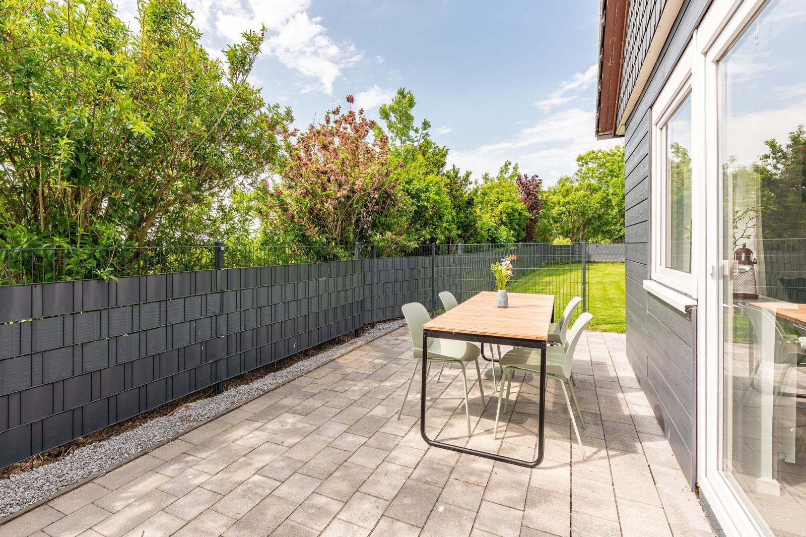 Terrace with table and chairs, surrounded by greenery and a black fence.