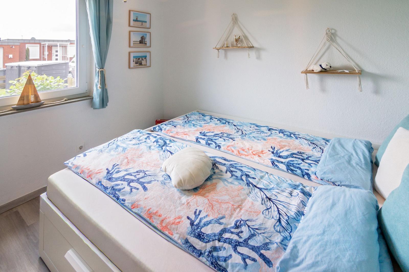 Schlafzimmer mit Doppelbett, Fenster und Wandregalen.