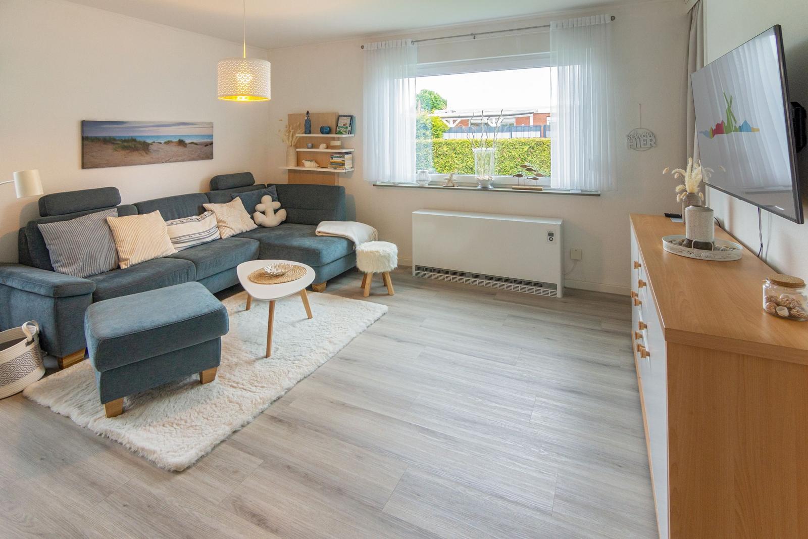 Ein Wohnzimmer mit grauem Sofa, Holzboden und großem Fenster.