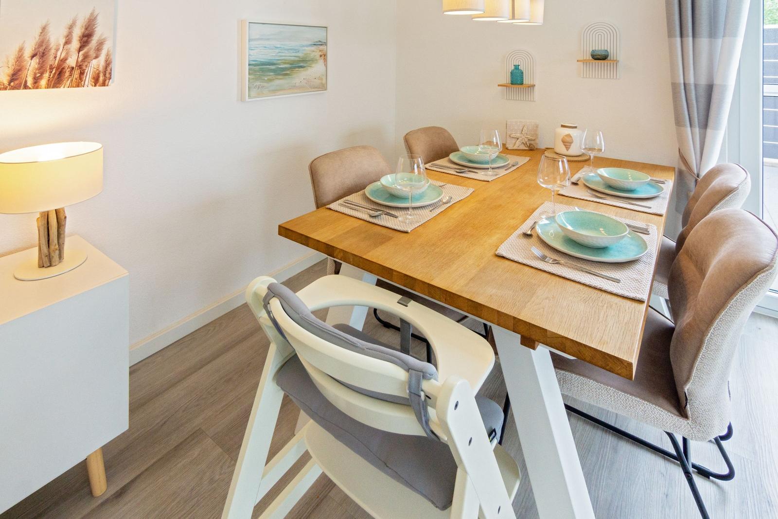 Esszimmer mit Holztisch, Stühlen und Kindersitz. Wandbild und Lampe sind sichtbar.