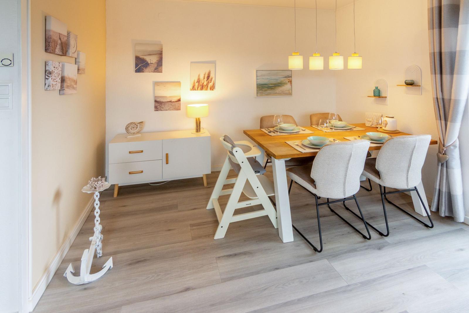 Esszimmer mit Holztisch, Stühlen und Wandbildern. Anker dekoriert den Boden.