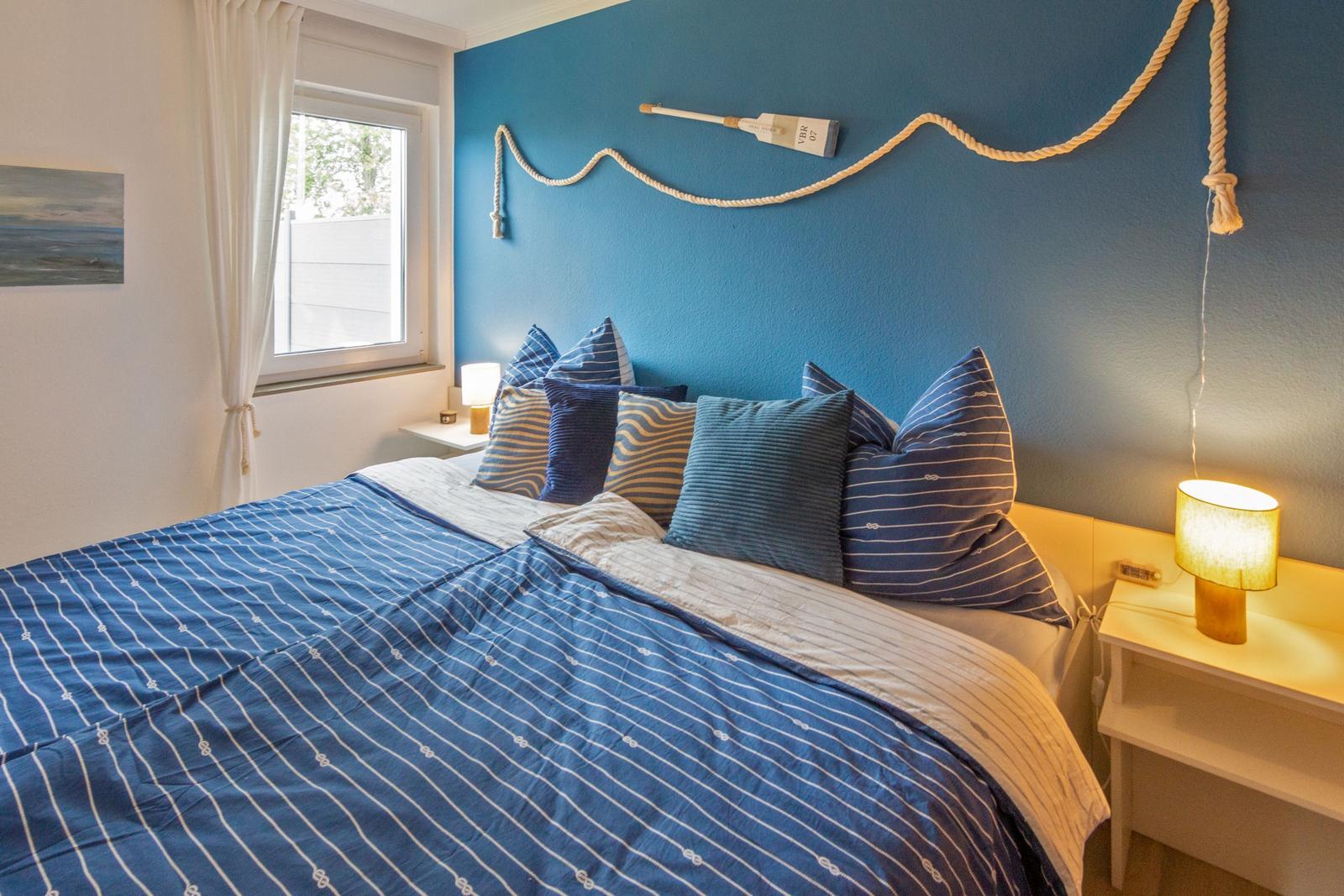 Schlafzimmer mit blauer Wand, Bett mit Kissen und Nachttisch mit Lampe.
