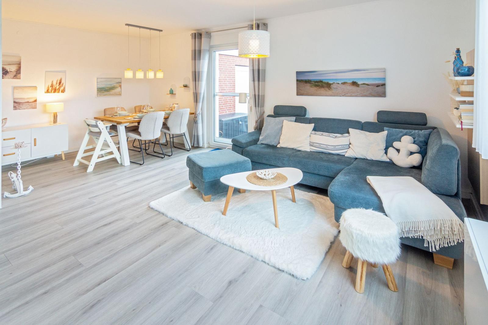 Wohn- und Essbereich mit Sofa, Tisch und Stühlen. Fenster zum Balkon. Wandbilder und Teppich.