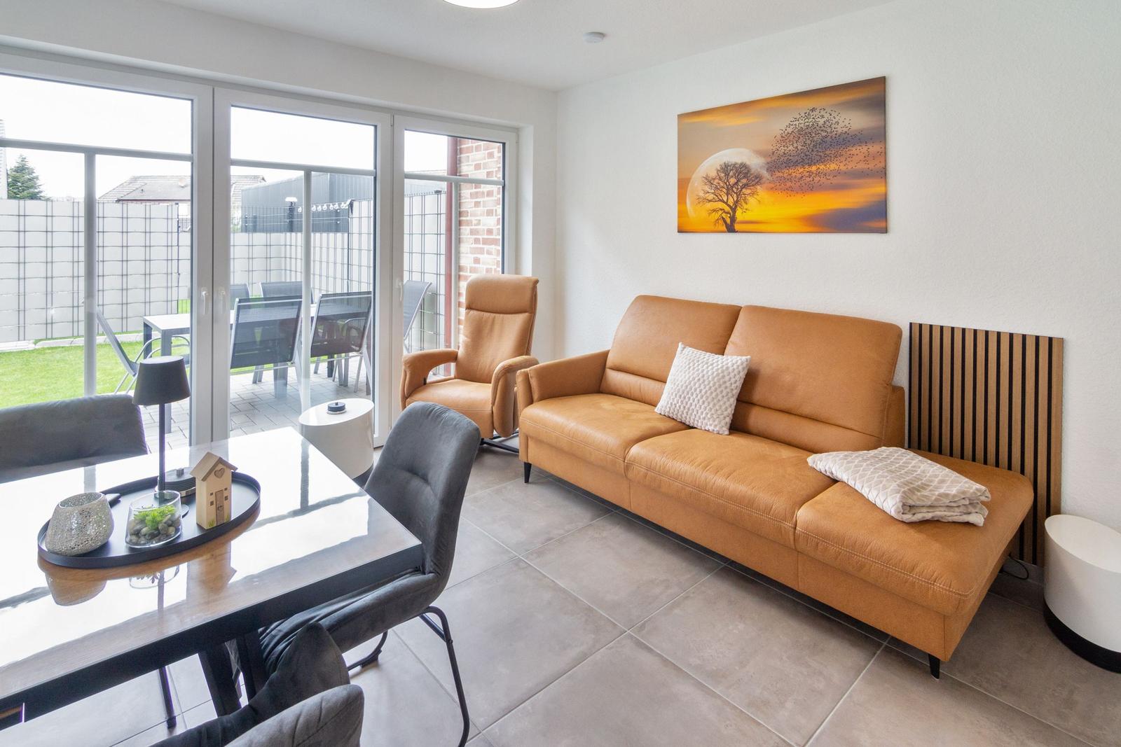 Wohn- und Essbereich mit braunem Sofa, Sitzgelegenheiten und Blick auf den Garten.