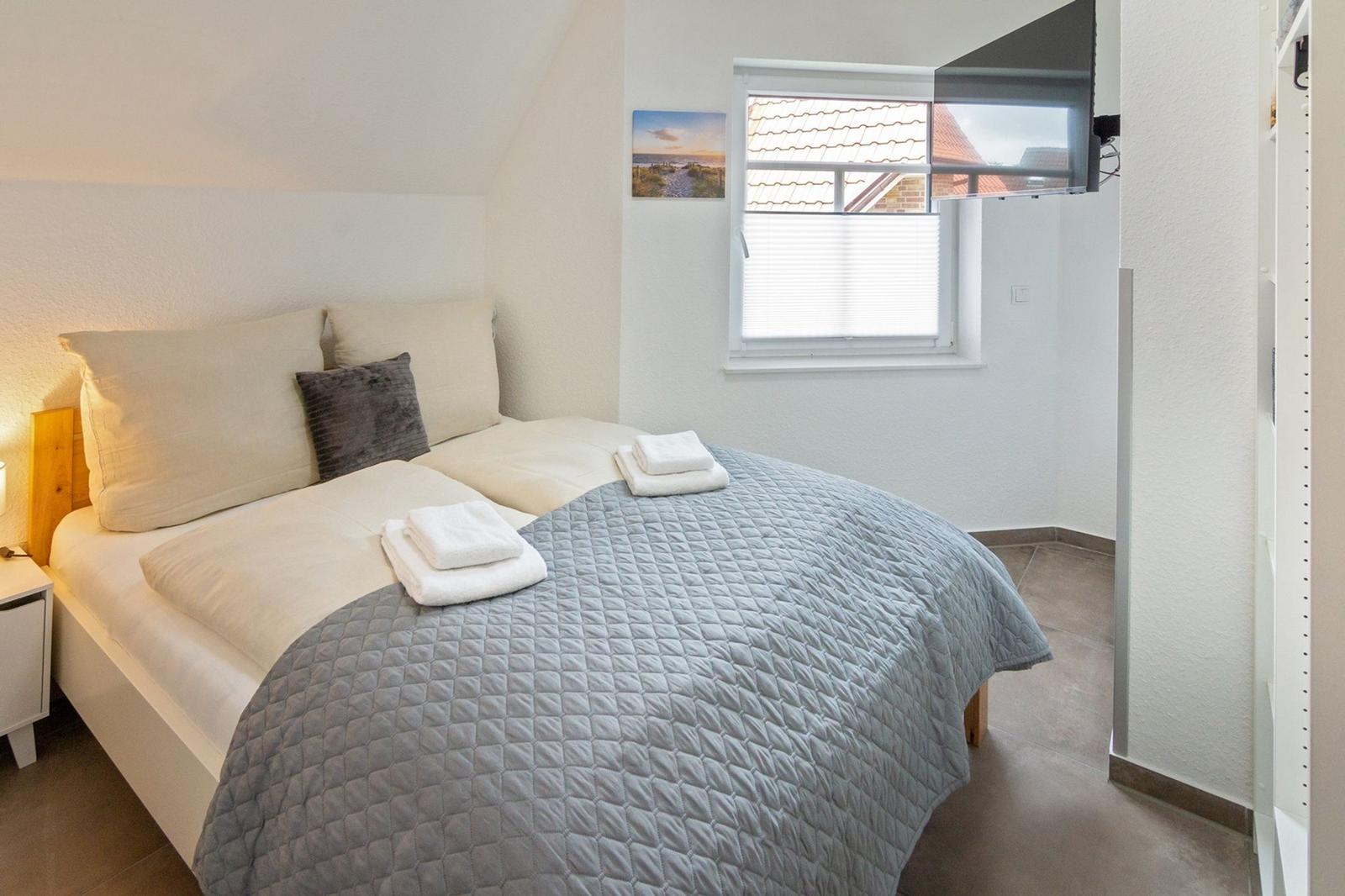 Ein Schlafzimmer mit Bett, Fenster und TV. Auf dem Bett liegen Handtücher.