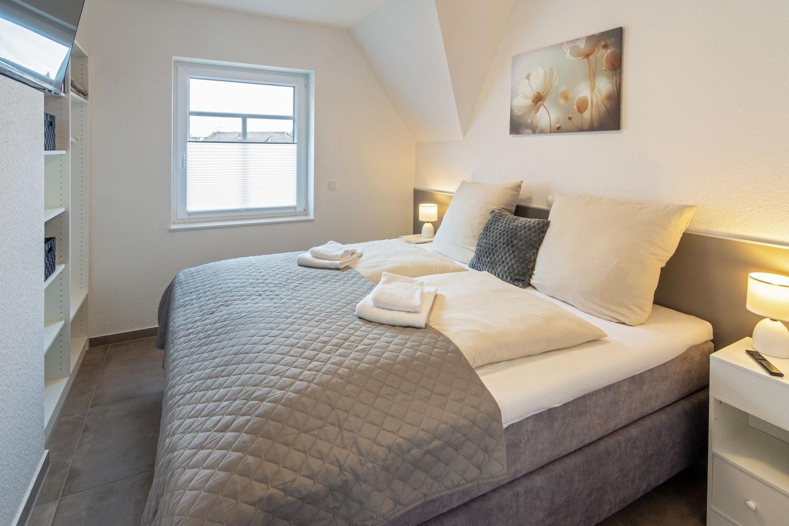 Schlafzimmer mit Doppelbett, Fenster und Nachttischen.