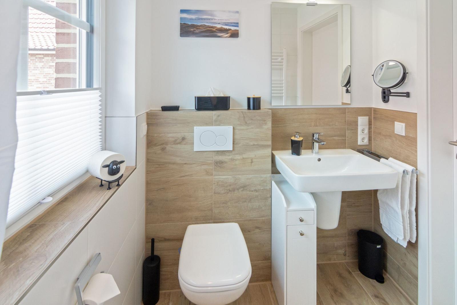 Badezimmer mit Waschbecken, Toilette und Fenster mit Jalousie.