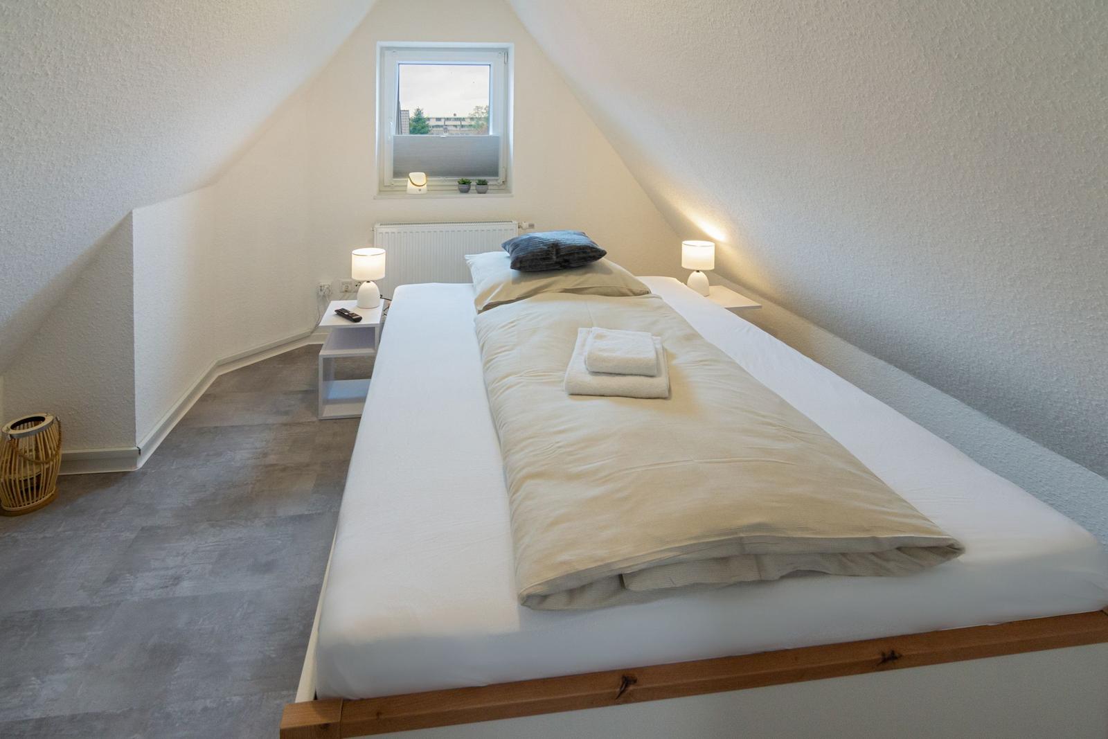 Schlafzimmer mit Dachschrägen, Bett, zwei Nachttischen und Fenster.