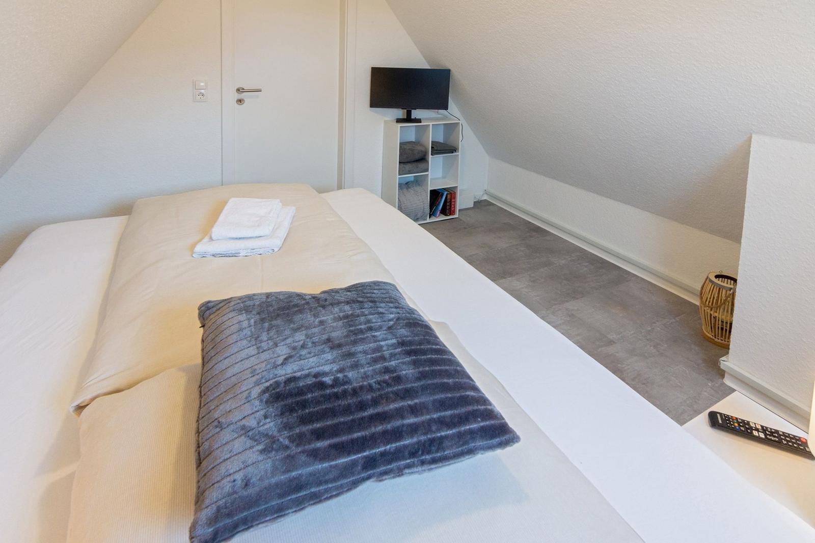 Schlafzimmer mit Bett, Fernseher und Regal unter Dachschräge.