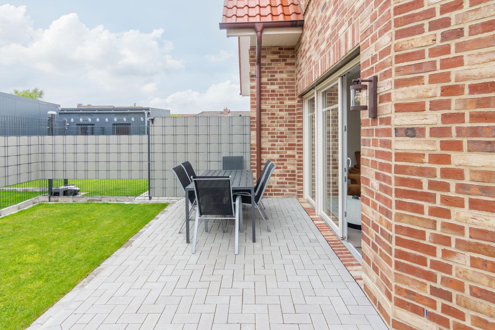 Terrasse mit Tisch und Stühlen, grüner Rasen und Backsteinmauer.