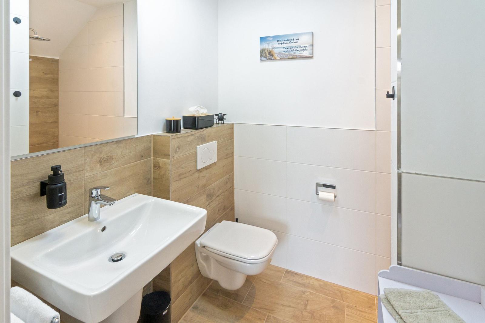 Badezimmer mit Waschbecken, Toilette und Dusche. Holzwand und Spiegel.