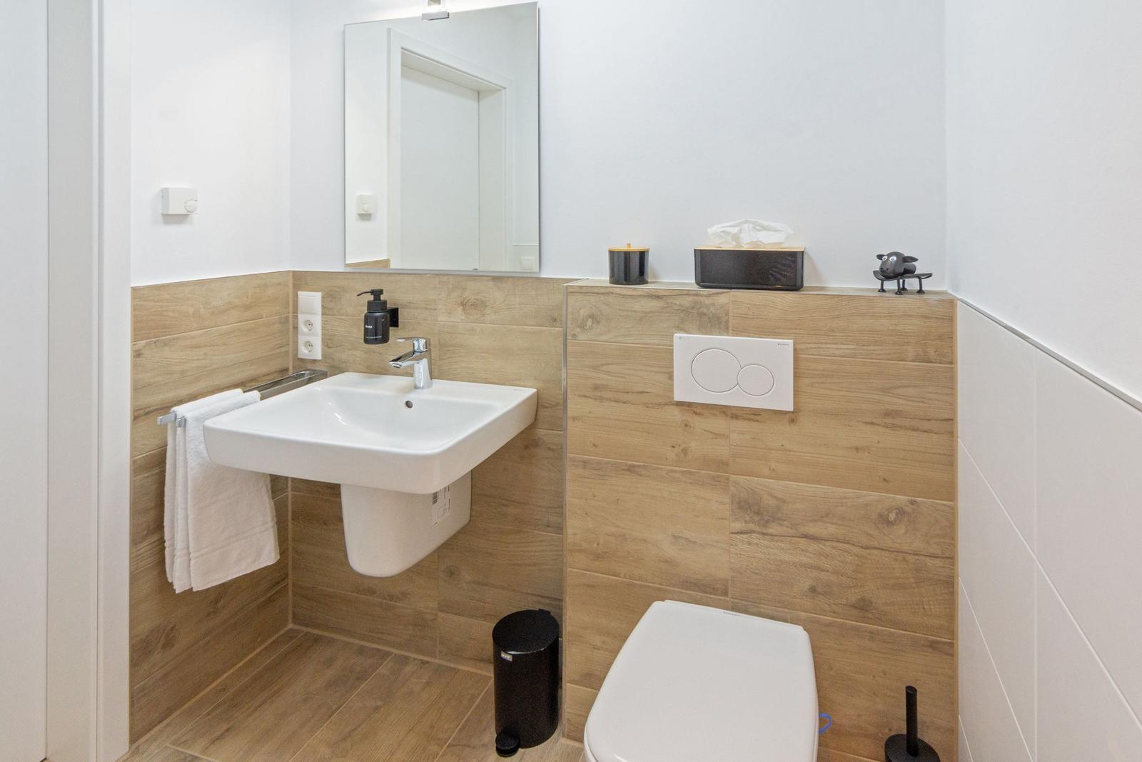 Badezimmer mit Waschbecken, Spiegel, Toilette und Holzverkleidung.