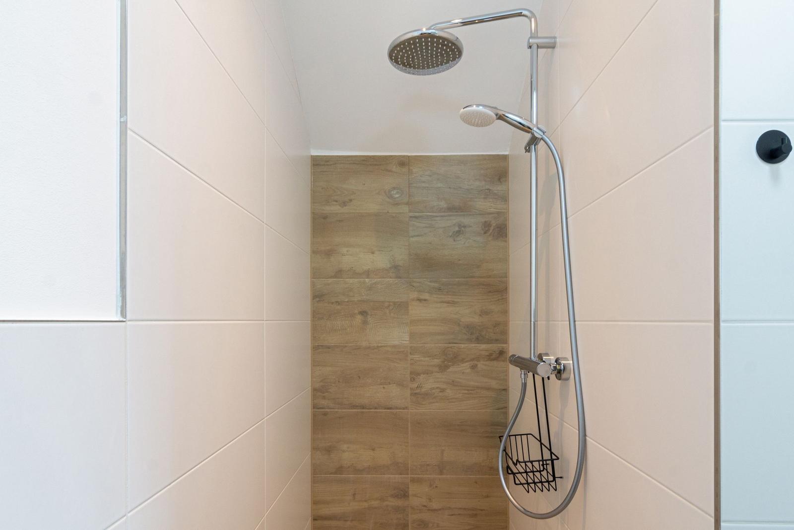 Dusche mit Duschbrause und Handbrause an Wand montiert.