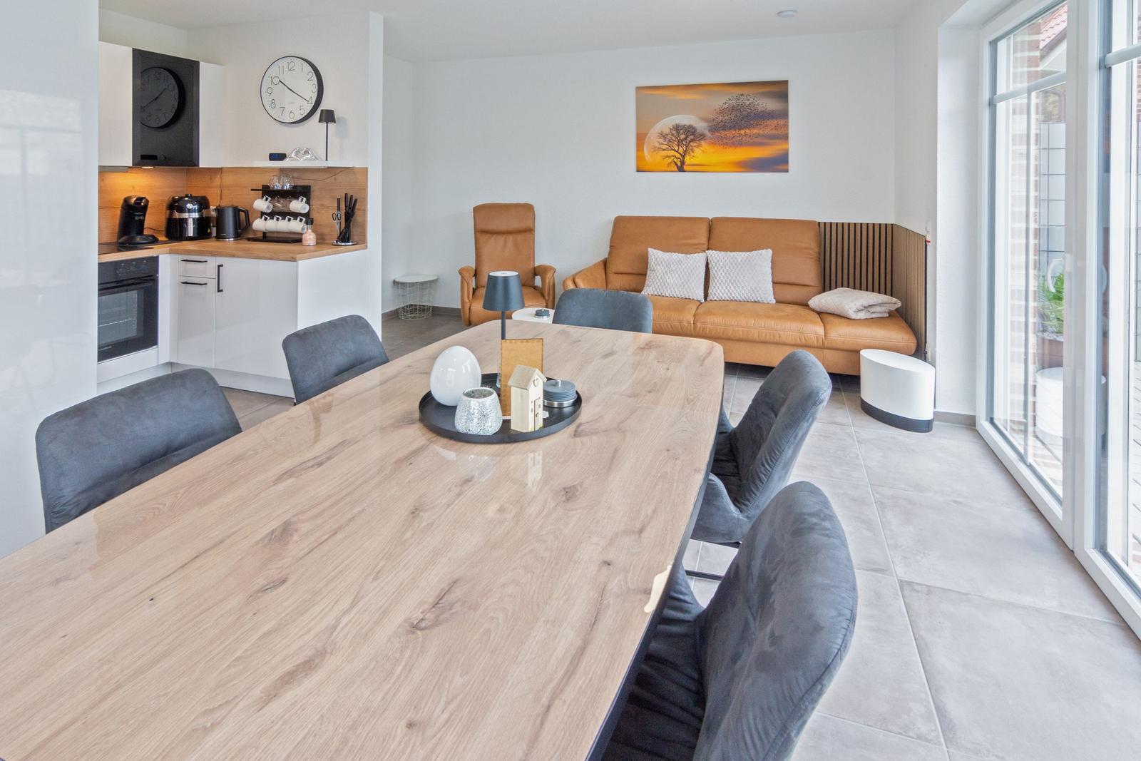 Großer Essbereich mit Holztisch und grauen Stühlen. Küche und Wohnbereich sind sichtbar.