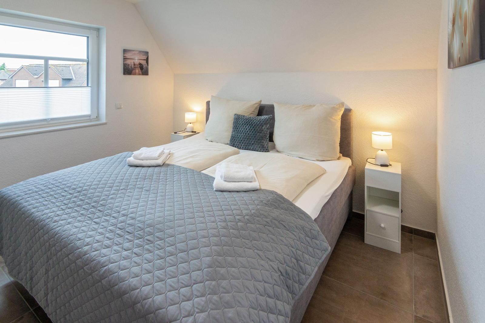 Schlafzimmer mit Doppelbett, Nachttischen und Fenster. Bett mit Bettwäsche und Kissen.