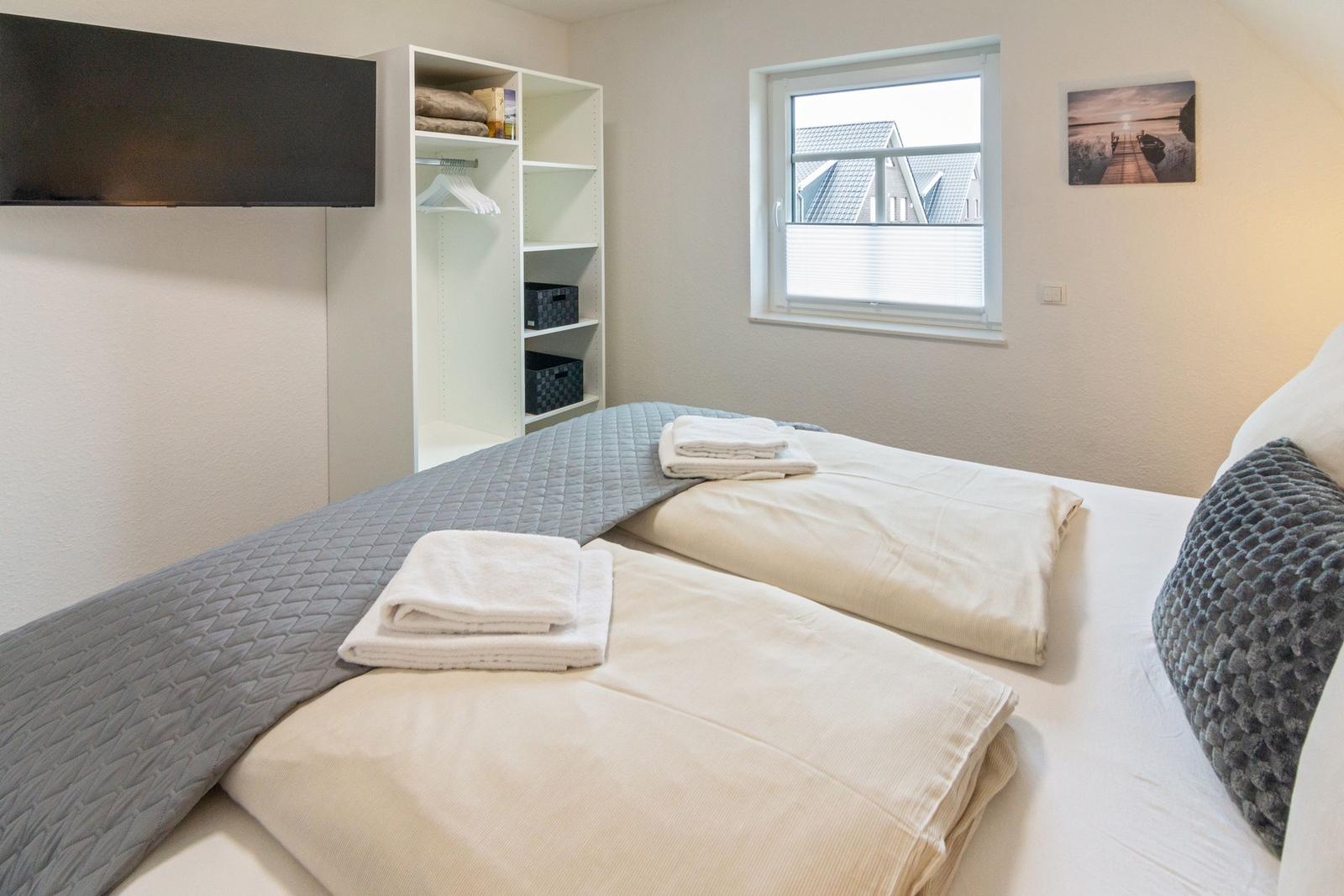 Schlafzimmer mit Bett, Kleiderschrank und Fenster. Auf dem Bett liegen Handtücher.