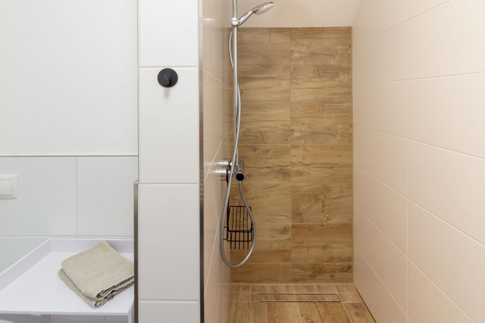 Dusche mit Holzoptik und Handbrause. Handtuch auf weißer Ablage.